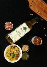 Ekaris Wood Pressed Groundnut Oil bottle placed next to bowl of poha, peanuts, chutney and spices on dark kitchen surface