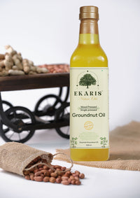 Ekaris Wood Pressed Single Pressed Groundnut Oil 1000ml bottle with raw peanuts in jute bag and vintage wooden cart in background